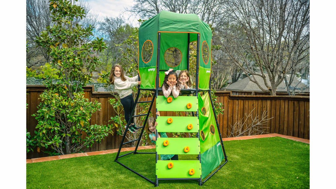 Three young girls posing on top of an outdoor climbing tower for kids. 